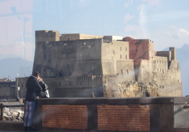 Castel dell'Ovo, seen through glass, frames the moment in Naples, Italy